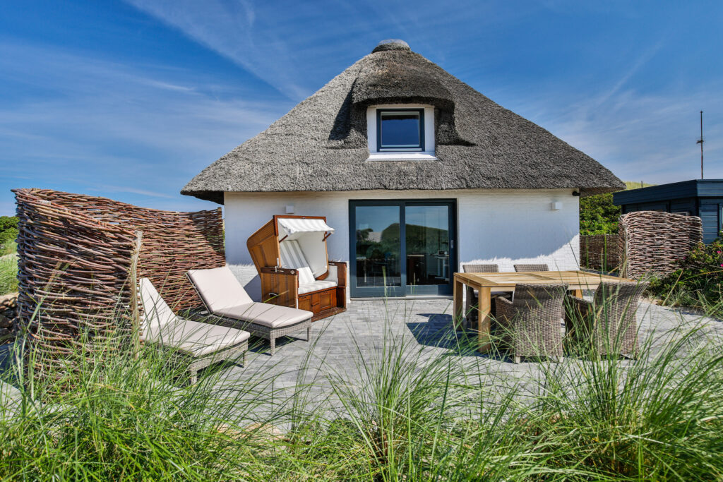 Strandhaus auf Sylt mit einem Reetdach und zwei Liegen und einem Strandkorb.