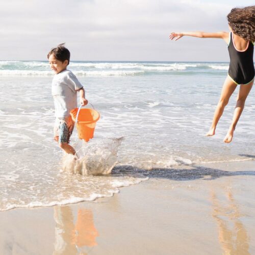 Zwei Kinder spielen im Wasser am Strand und springen herum.