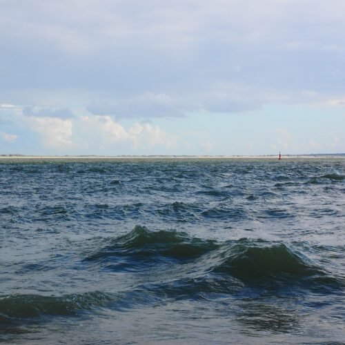 Das Meer, imHintergrund die Küste mit blauen Himmel und vielen hellen Wolken.