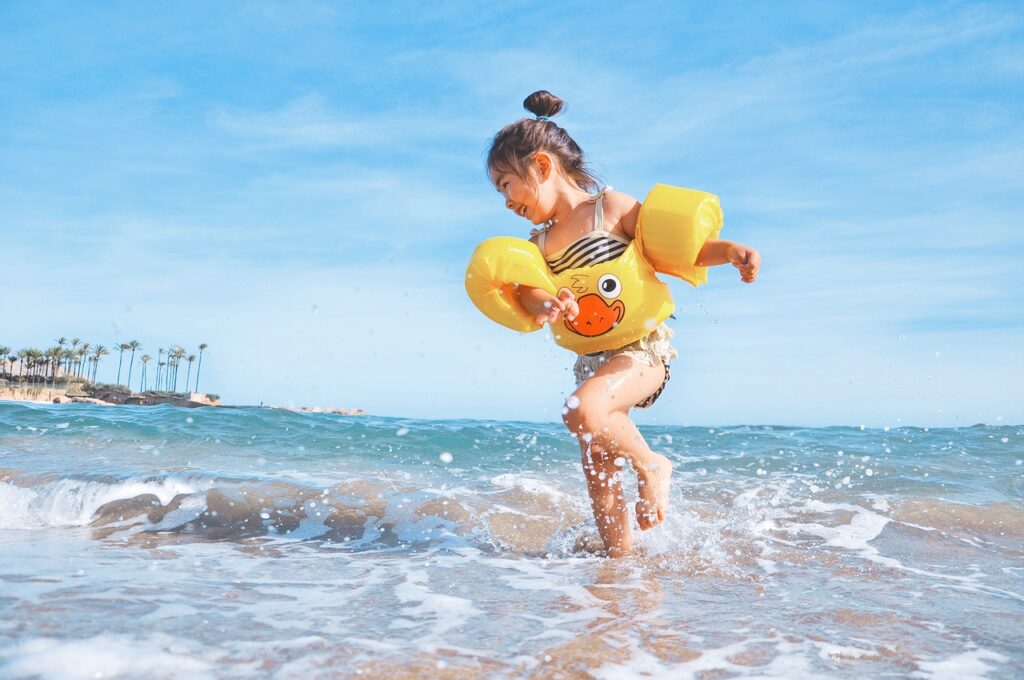 Kind mit schwimmflügel plantscht im Wasser am sylter Strand bei Sonnenschein und blauen Himmel.