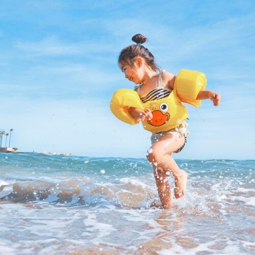 Kind mit schwimmflügel plantscht im Wasser am sylter Strand bei Sonnenschein und blauen Himmel.
