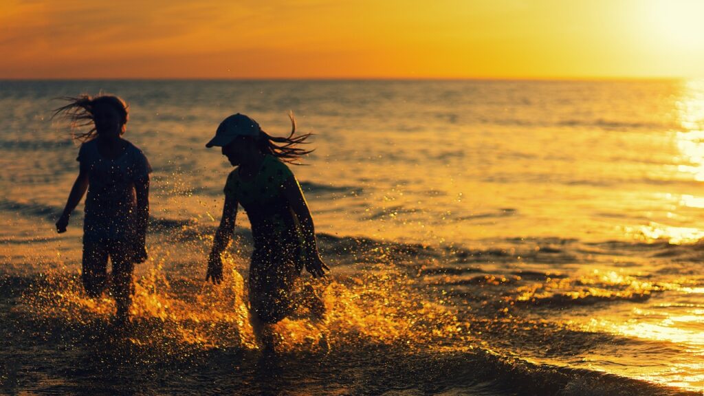 Kurzurlaub auf Sylt. Zwei Personen im Wasser bei Sonnenuntergang. die Eine Person hat eine Cap auf. Das Wasser erstrahlt in einem Gelb-Gold durch die untergehende Sonne.