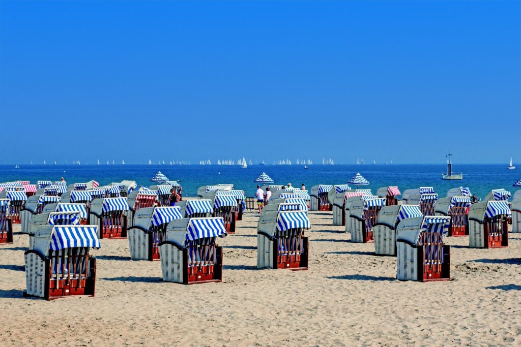 Strandkörbe auf Sylt. im Hintergrund das blaue Meer mit mindestens 20 weißen Segelschiffen am Horizont. es ist Sonnenschein und es ist keine einzige Wolke zu sehen.