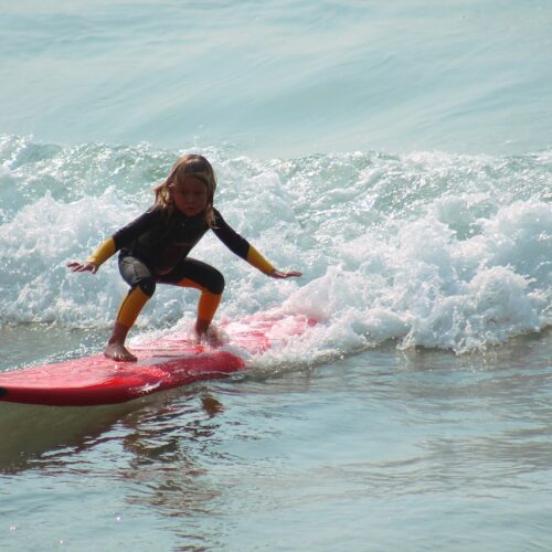 Kind surft auf einem roten Surfbrett.