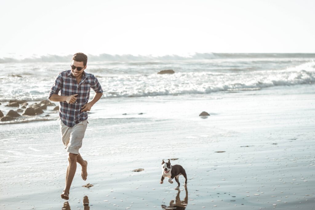 Mann läuft mit Hund am Strand entlang