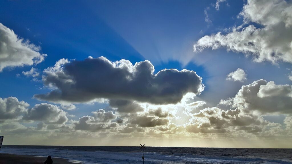 Sonne und Wolken an der Küste von Sylt. Eine Wolke verdeckt die Sonne bei blauem Himmel.