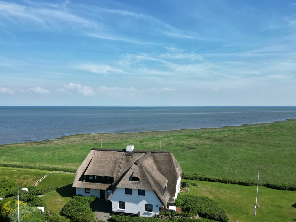 Vogelperspektive auf Reetdachhaus auf Sylt in der grünen Landschaft am Meer