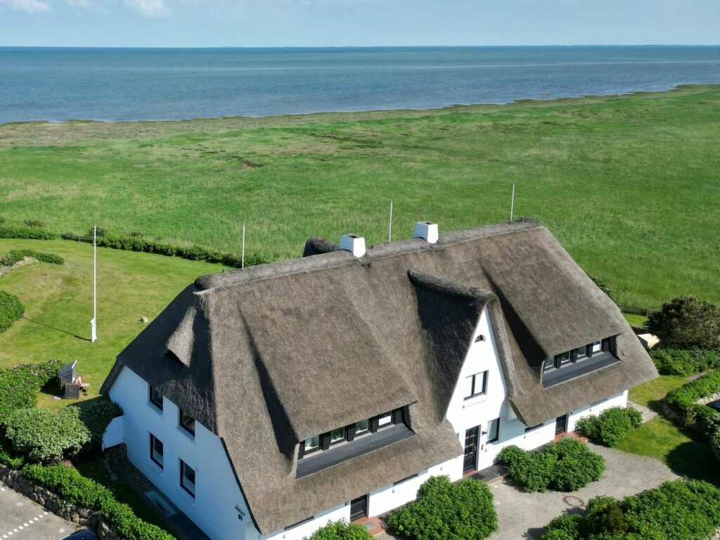 Blick von oben auf großes Reetdachhaus am Meer auf Sylt