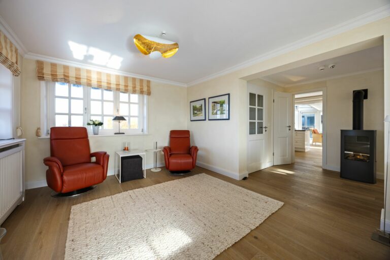 Wohnzimmer mit zwei roten Sesseln einem großen Teppich und einen Kamin in Ferienwohnung auf Sylt