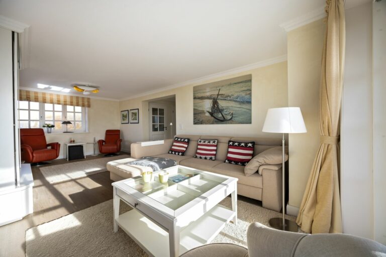 Wohnzimmer mit einem Couchtisch, einem Sofa, einem Sessel und zwei roten Sesseln in Ferienwohnung auf Sylt