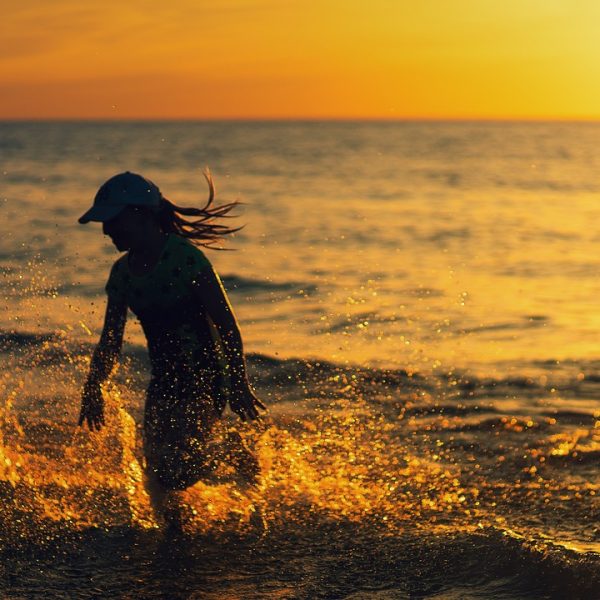 Kurzurlaub auf Sylt. Zwei Personen im Wasser bei Sonnenuntergang. die Eine Person hat eine Cap auf. Das Wasser erstrahlt in einem Gelb-Gold durch die untergehende Sonne.